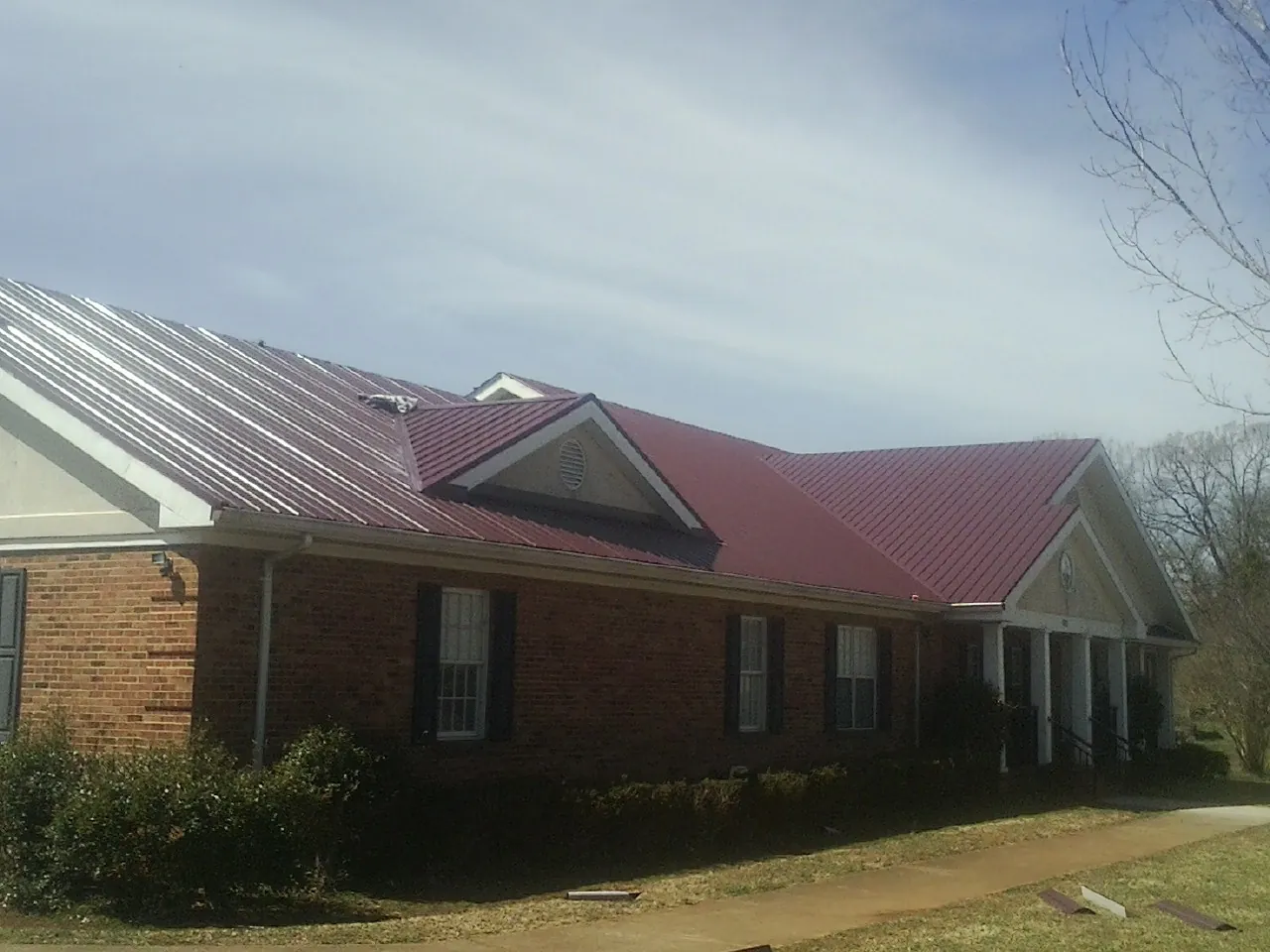 Red metal roof with gabled entries on a long brick building, from a Hail Damage Roof Repair job in Centralia