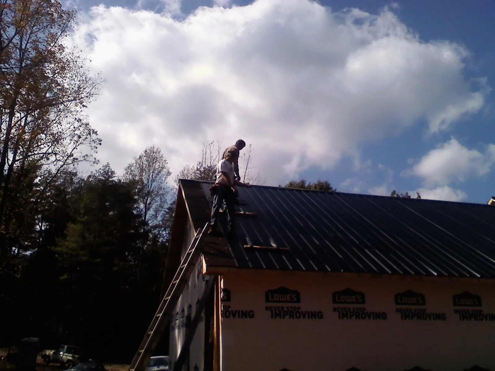 Roofer fastening dark metal panels high against a cloudy sky, from a Roof Inspection job in Centralia